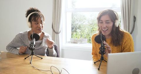 Two women co-hosting podcast recording lively conversation with laptop and tabletop mics