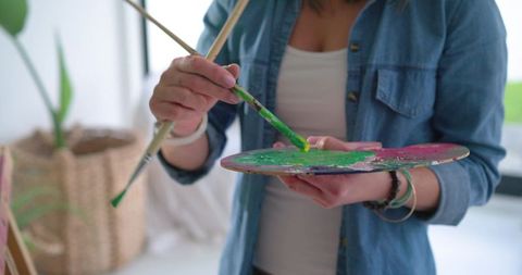 Woman Mixing Green Paint on Palette in Bright Studio Wearing Denim Shirt