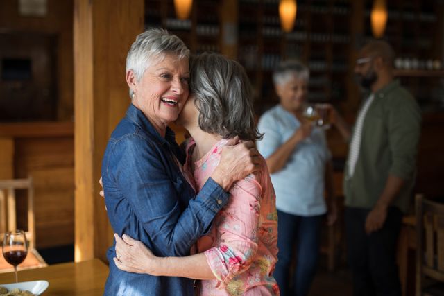 Senior women embracing in a bar, showcasing friendship and joy. Ideal for use in advertisements promoting social activities for seniors, lifestyle blogs, or content focused on friendship and bonding among elderly individuals.