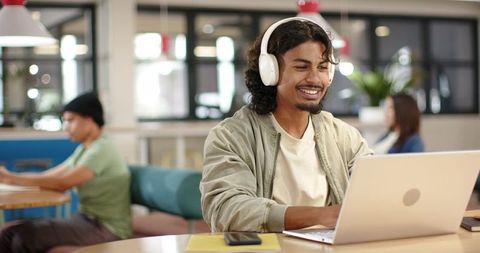 Young man wearing headphones working on laptop in bright modern coworking cafe