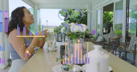 Asian woman talking at sunroom table with colorful data infographics for modern lifestyle