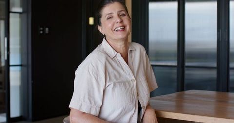 Confident mature woman leaning and smiling at wooden table in modern corporate boardroom