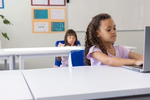 African american and asian students using laptop focused on digital learning at desks