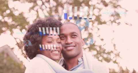 Smiling couple cuddling under blanket in park with soft bokeh and digital data overlay
