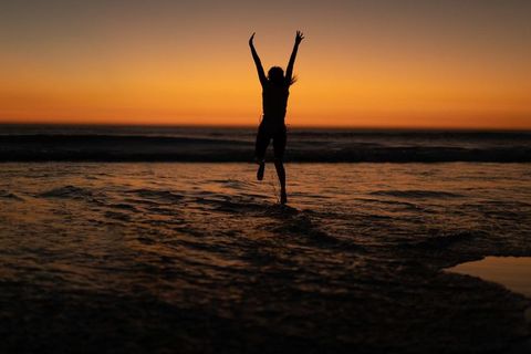 African American Male Jumping Shoreline at Golden Sunset Silhouette Ocean Reflection