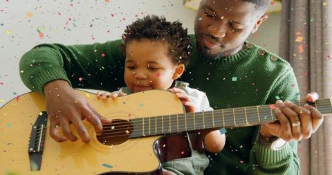 Father teaching baby to play acoustic guitar at home, intimate parent-child music bonding