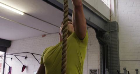 Man climbing rope in gym wearing lime green shirt showing strength and determination