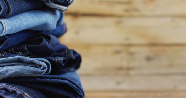 Several pairs of jeans neatly folded and stacked against a rustic wooden background. Ideal for use in fashion blogs, retail clothing advertisements, and lifestyle magazines to showcase casual wear or clothing organization tips.