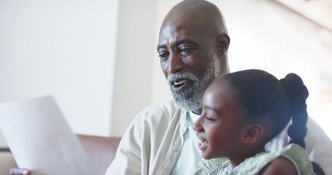 Grandfather sharing letter with granddaughter, smiling intergenerational bonding at home