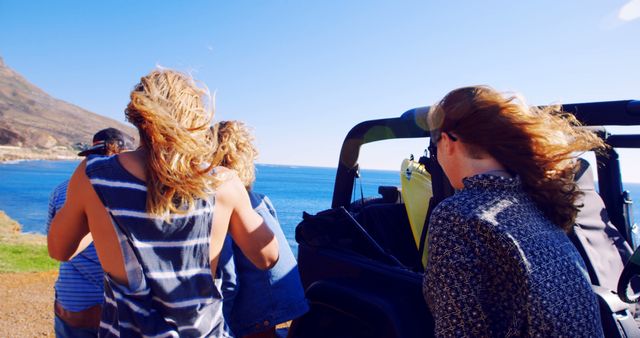 Group of friends enjoying a scenic road trip along the coast, riding in a convertible vehicle. Perfect for travel blogs, advertisements for road trips, leisure activities, and summer vacation promotions.