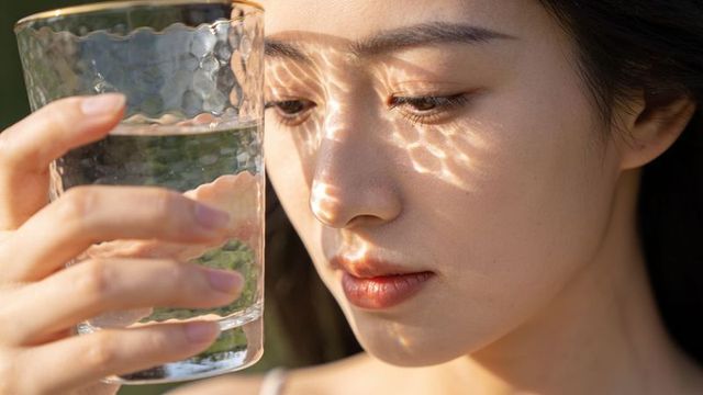 Asian woman holding textured glass, sunlit water reflections dancing on face portrait