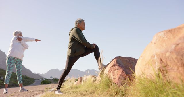 Senior man and woman stretching in a picturesque mountain location, embodying active and healthy lifestyles. Ideal for illustrating wellness in older age, promoting outdoor exercise, and adventurous fitness routines. Great for health articles, fitness guidelines for seniors, and advertisements for activewear.