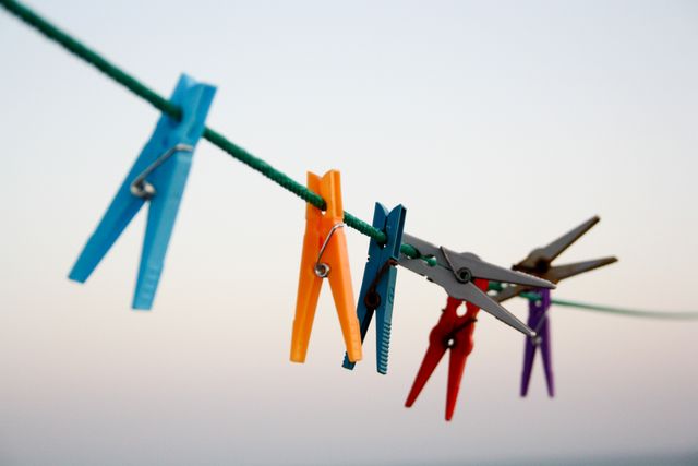 Array of vibrant clothespins attached to a clothesline under a clear sky. Perfect image for depicting daily chores, outdoor laundry scenes, simplicity of everyday tasks, or concepts of airing and drying. Useful for blog posts about home life, advertisements for household laundry supplies, or websites focused on environmental outdoor activities.