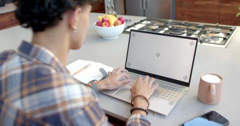 Man working on laptop at kitchen counter with coffee and fruit bowl for home productivity