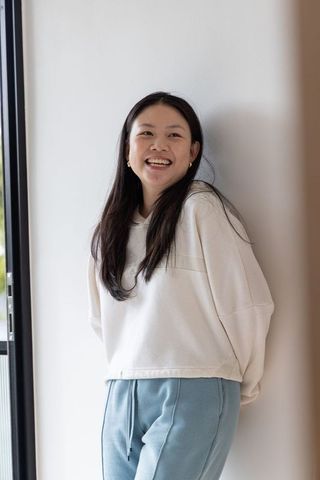 Smiling asian woman leaning by white wall in casual loungewear with gold hoops
