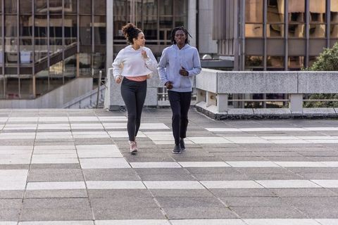 Diverse women jogging on urban terrace plaza wearing hoodies and leggings for fitness