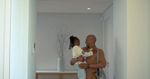 Father carrying daughter through modern foyer smiling and sharing affectionate moment
