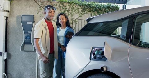 African American Friends Charging Electric Vehicle at Modern Home