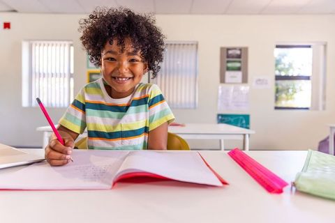 Smiling african american boy writing in notebook at bright classroom desk