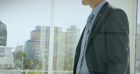Executive standing at office window gazing at urban skyline reflecting corporate ambition