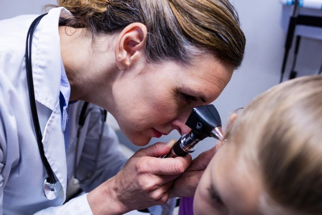 Female doctor using otoscope to examine patient's ear in hospital. Ideal for healthcare, medical examination, pediatric care, and professional medical services themes. Useful for articles, blogs, and educational materials on ear health and medical checkups.