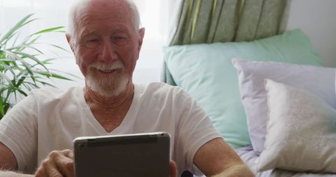 Senior Man Using Tablet in Bedroom for Social Connection