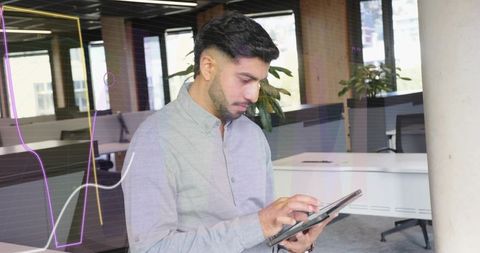Indian man using tablet in modern open office tapping screen and reviewing analytics