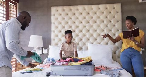 African American parents packing suitcase while child watches on bed planning family trip