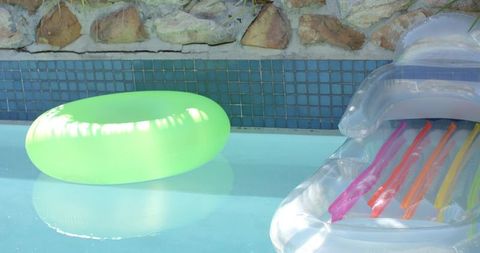 Neon green swim ring floating in sunlit backyard pool next to transparent striped lounger