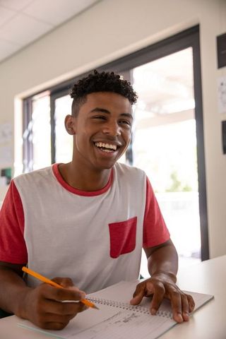Teen boy smiling sketching in notebook at sunlit workspace