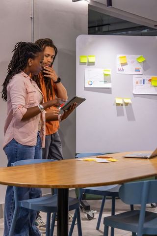 Colleagues reviewing tablet and sticky-note board in modern office brainstorming session