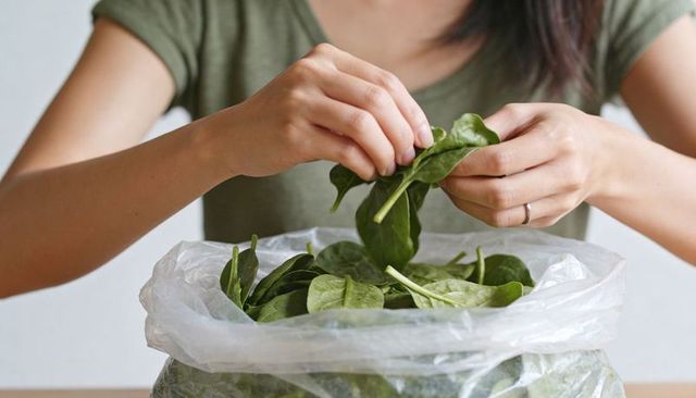 Woman preparing fresh spinach leaves by hand for salad, home cooking, healthy meal prep