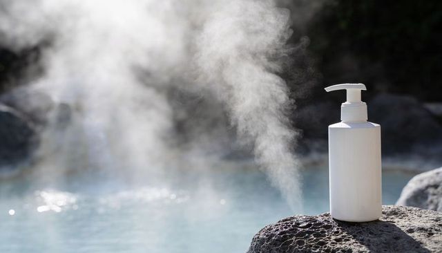 White pump bottle on volcanic rock beside steaming hot spring, natural spa product display