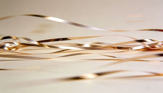 Shimmering gold and bronze foil ribbons curving across pale beige minimalist surface