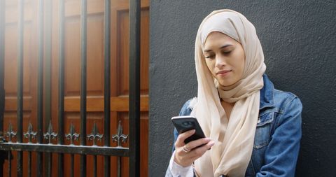 Young Woman in Hijab Using Smartphone Outside Urban Building