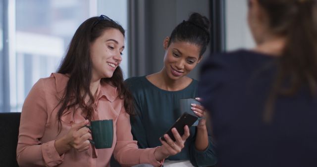 Diverse Young Women Smiling and Looking at Smartphone in Office - Download Free Stock Images Pikwizard.com