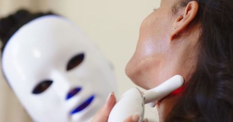 African american woman receiving led neck therapy with white mask device at spa clinic