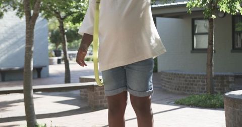 Teen spinning yellow hula hoop in sunlit plaza wearing oversized tee and rolled jean shorts