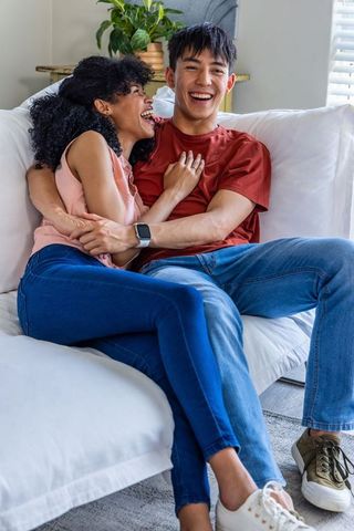Laughing diverse couple cuddling on modern sofa at home conveying cozy everyday intimacy
