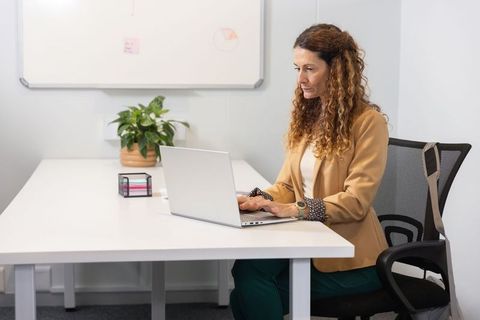 Mature professional woman typing on laptop at minimalist office desk with green plant