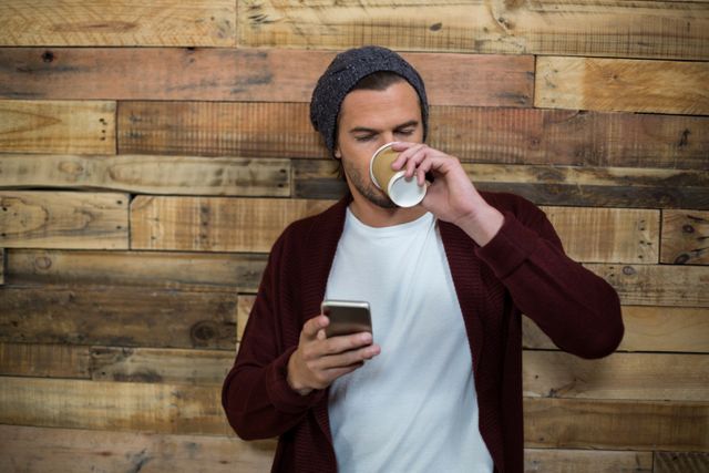 Man using mobile phone while having a coffee against wooden wall