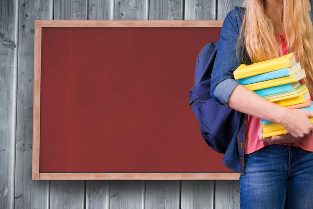 Student carrying books and wearing a backpack, standing next to a blank chalkboard with wooden wall background. Suitable for educational content, school advertisements, back-to-school promotions, and learning environments. Can be used in materials promoting literacy, academic subjects or educational institutions.