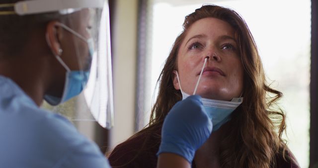 Nurse in protective gear conducting a nasal swab test on a woman for COVID-19 testing purposes. Ideal for use in health-related articles, pandemic-related information, and medical brochures.