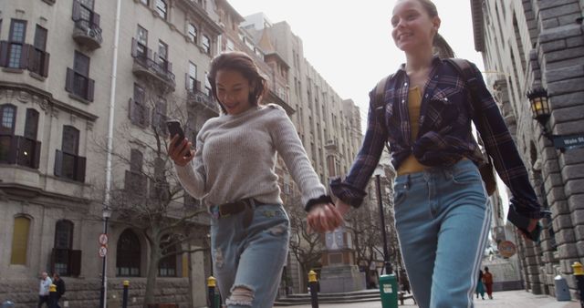 Diverse girl friends walking holding hands in city, copy space. Summer, friendship, on the go, city and lifestyle concept, unaltered.