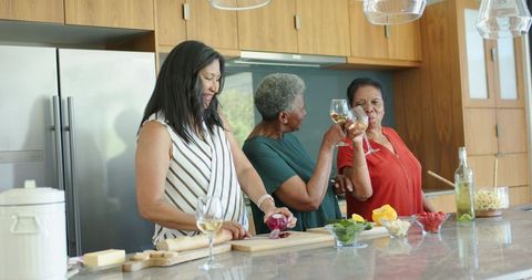 African american women toasting wine while preparing dinner and sharing laughter on kitchen island