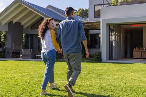 Young couple walking hand-in-hand toward modern two-story home holding key fob