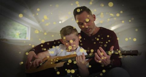 Father Guiding Son in Guitar Playing with Sparkling Overlay