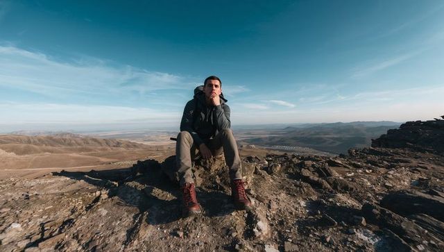 Solo hiker sitting on rocky summit gazing over expansive valley with red boots and pack