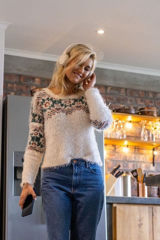 Young woman listening to music in cozy rustic kitchen wearing fluffy nordic sweater smiling