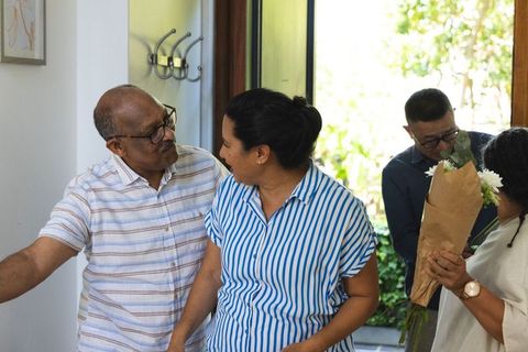 Family arriving home greeting senior couple with bouquet in sunny foyer